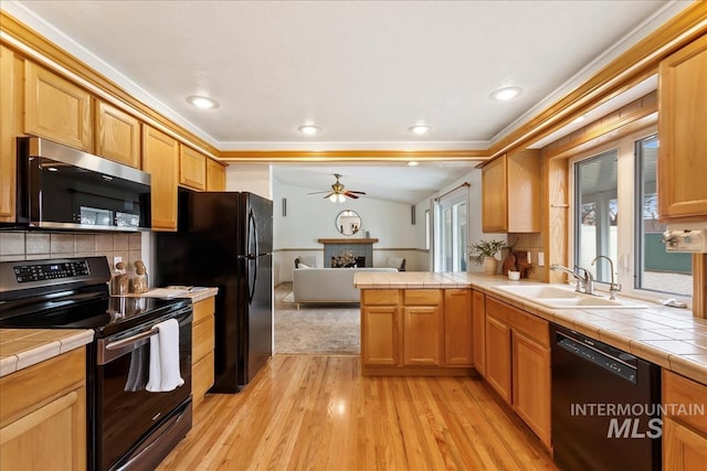 kitchen with tile counters, light wood-style flooring, black appliances, a fireplace, and a sink