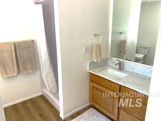 bathroom featuring wood finished floors, baseboards, toilet, vanity, and a shower with curtain