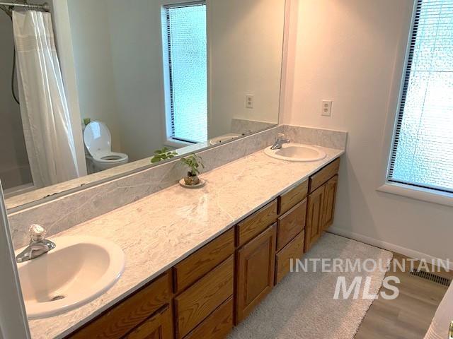 bathroom featuring double vanity, curtained shower, baseboards, and wood finished floors