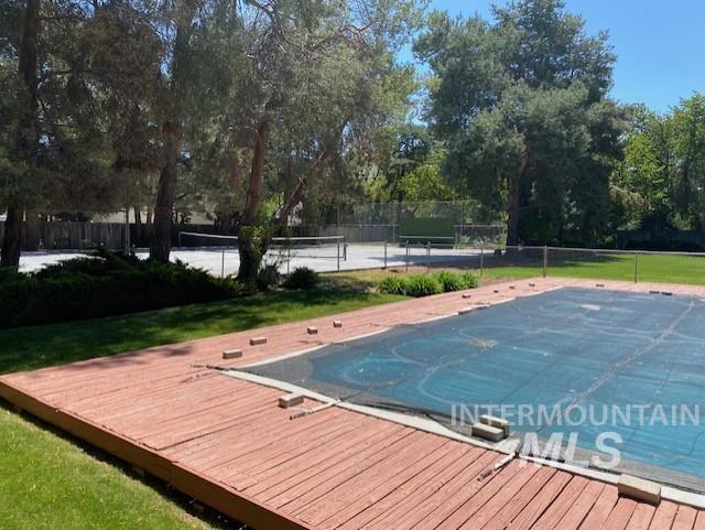 view of swimming pool featuring a tennis court, fence, and a wooden deck
