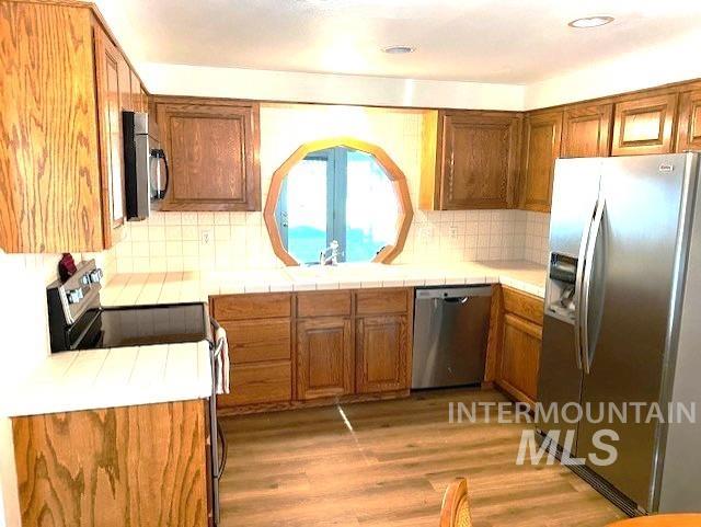 kitchen with appliances with stainless steel finishes, brown cabinets, light wood-type flooring, tasteful backsplash, and recessed lighting