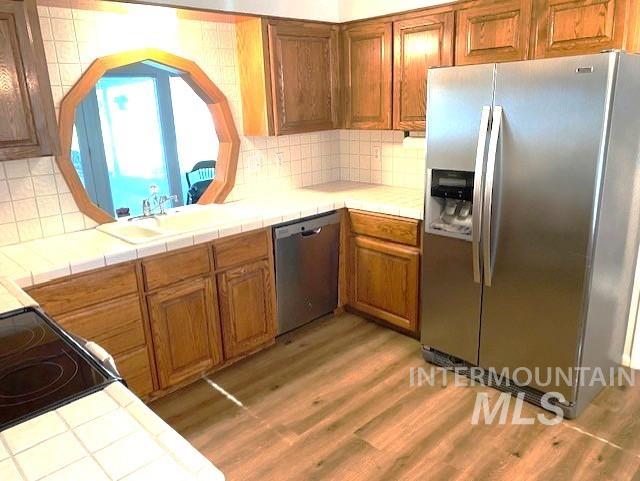 kitchen with stainless steel appliances, tile counters, brown cabinets, and light wood-style floors
