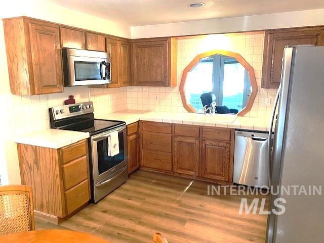 kitchen featuring appliances with stainless steel finishes, light wood-style floors, backsplash, brown cabinets, and a sink