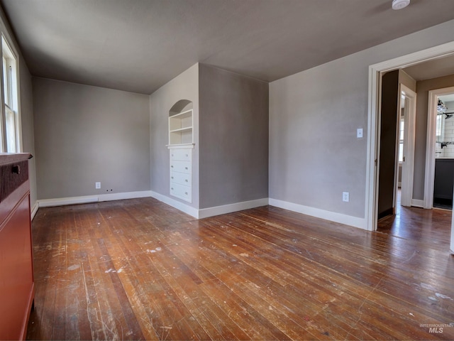 unfurnished room with built in shelves, dark wood-type flooring, and a wealth of natural light