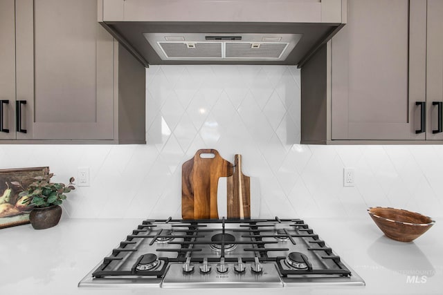 details featuring backsplash, gray cabinets, extractor fan, and stainless steel gas stovetop