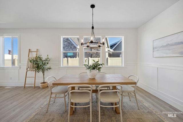 dining area featuring light wood finished floors, a wainscoted wall, a notable chandelier, and a decorative wall