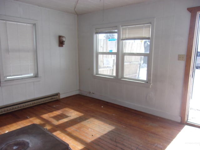 empty room featuring baseboard heating, plenty of natural light, and hardwood / wood-style flooring