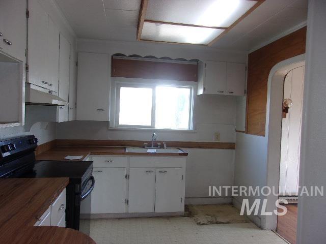 kitchen featuring light floors, black electric range oven, white cabinets, a sink, and under cabinet range hood