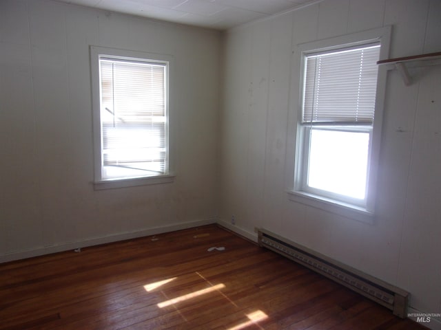 empty room featuring baseboards, a baseboard heating unit, and dark wood-type flooring