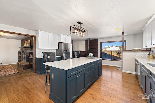 kitchen featuring decorative backsplash, appliances with stainless steel finishes, light wood-type flooring, decorative light fixtures, and white cabinetry