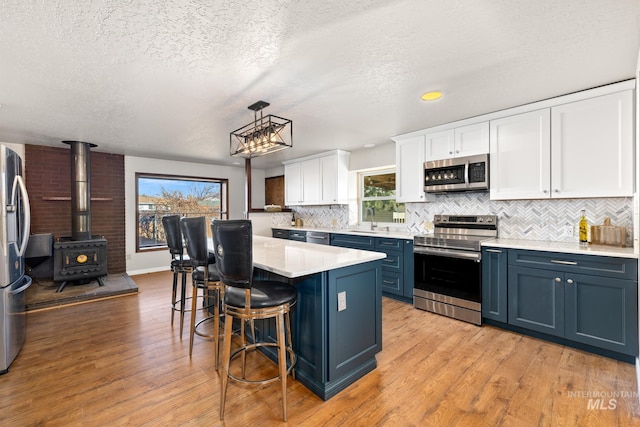 kitchen with a wood stove, hanging light fixtures, blue cabinetry, white cabinetry, and stainless steel appliances