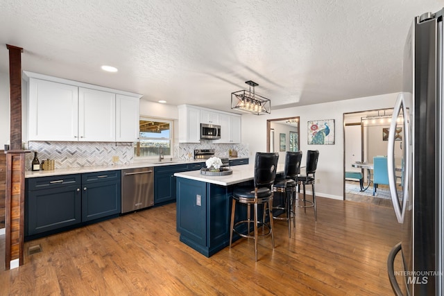 kitchen with a breakfast bar, stainless steel appliances, blue cabinets, white cabinets, and dark hardwood / wood-style floors