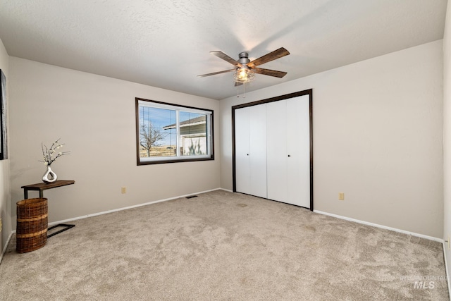 unfurnished bedroom featuring a textured ceiling, ceiling fan, light carpet, and a closet