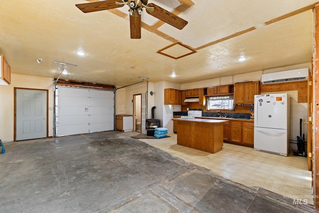 kitchen with a wood stove, a center island, a wall unit AC, a textured ceiling, and white appliances