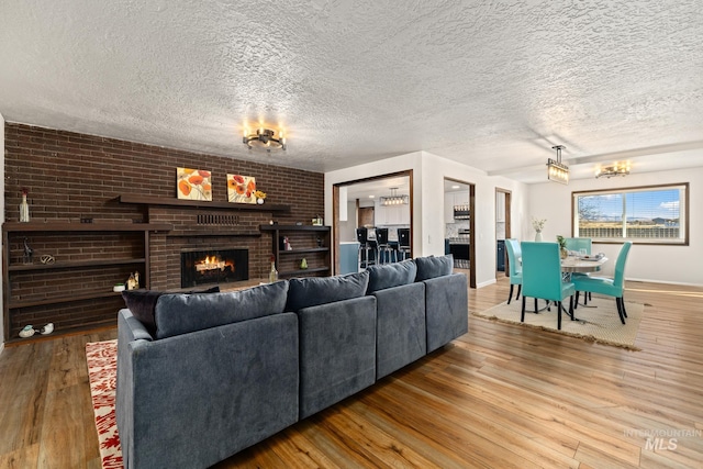 living room with an inviting chandelier, wood-type flooring, a textured ceiling, and a brick fireplace