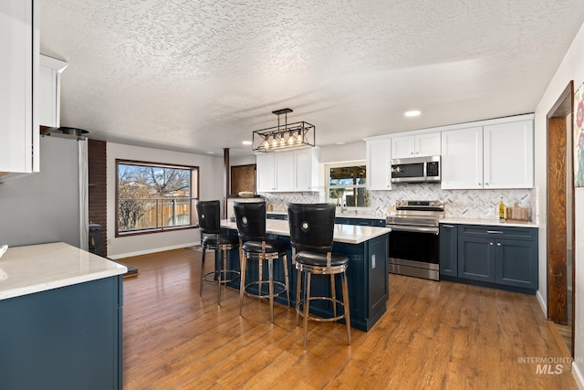 kitchen featuring dark hardwood / wood-style flooring, white cabinets, hanging light fixtures, and appliances with stainless steel finishes