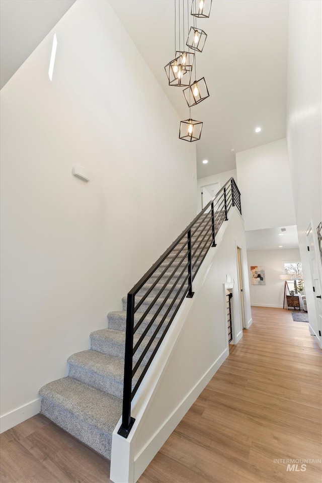 stairway with recessed lighting, a high ceiling, wood finished floors, baseboards, and an inviting chandelier