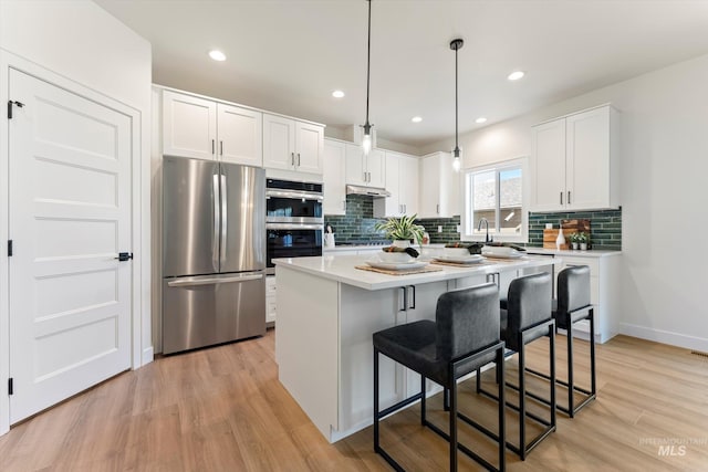 kitchen with light countertops, light wood-style flooring, appliances with stainless steel finishes, white cabinetry, and a kitchen bar