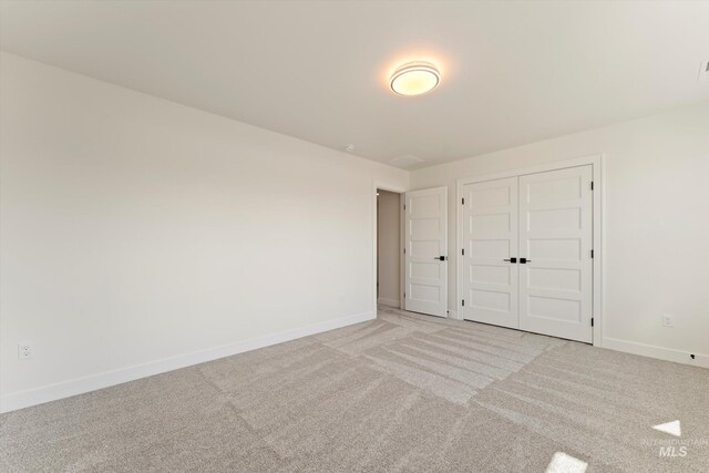 unfurnished bedroom with a closet, light colored carpet, and baseboards