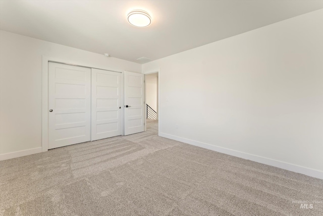 unfurnished bedroom with a closet, light carpet, and baseboards