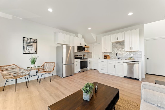 kitchen featuring stainless steel appliances, white cabinets, light countertops, backsplash, and light wood finished floors