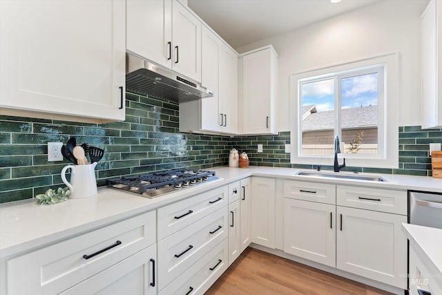 kitchen with stainless steel appliances, light countertops, white cabinets, a sink, and under cabinet range hood