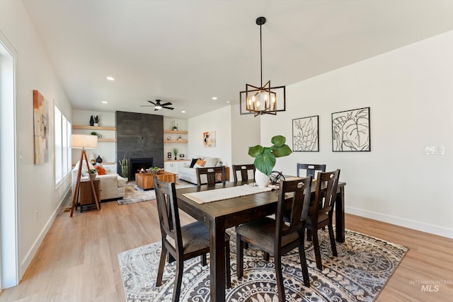 dining space featuring a tile fireplace, light wood-style flooring, recessed lighting, ceiling fan with notable chandelier, and baseboards