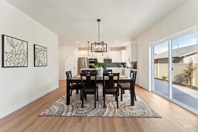 dining space with baseboards, light wood finished floors, recessed lighting, and an inviting chandelier