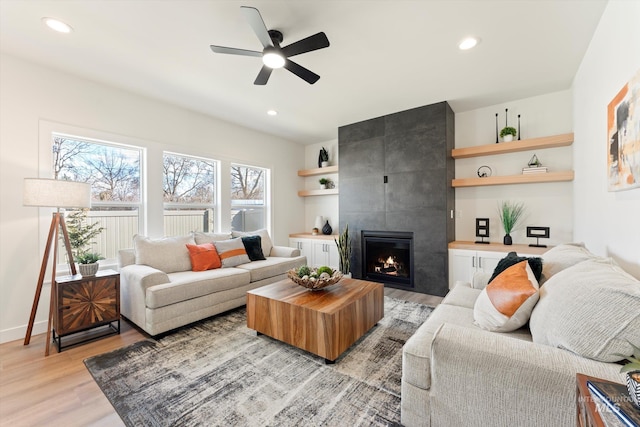 living room with recessed lighting, light wood-style floors, ceiling fan, a tile fireplace, and baseboards