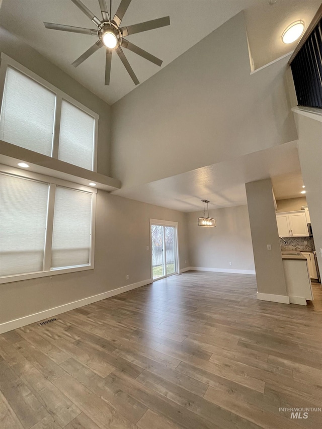 unfurnished living room with visible vents, wood finished floors, a towering ceiling, and baseboards