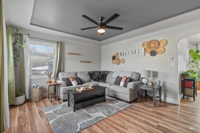 living room with a raised ceiling, ceiling fan, and light hardwood / wood-style floors