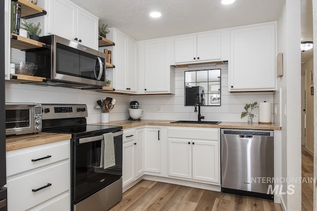 kitchen with white cabinets, a toaster, wooden counters, stainless steel appliances, and open shelves