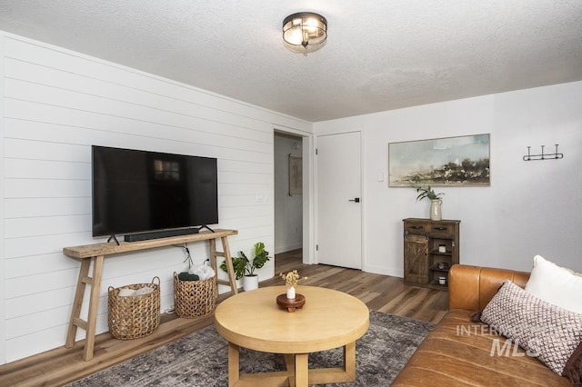 living area featuring wooden walls, baseboards, wood finished floors, and a textured ceiling