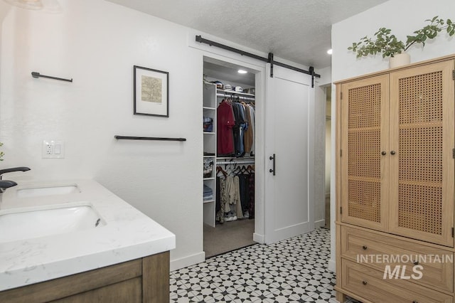 bathroom featuring tile patterned floors, a sink, a textured ceiling, and a walk in closet