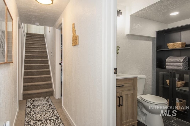 half bathroom with a textured ceiling, toilet, baseboards, a textured wall, and vanity
