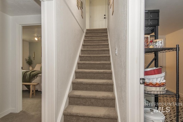 staircase featuring a textured wall, baseboards, and carpet floors