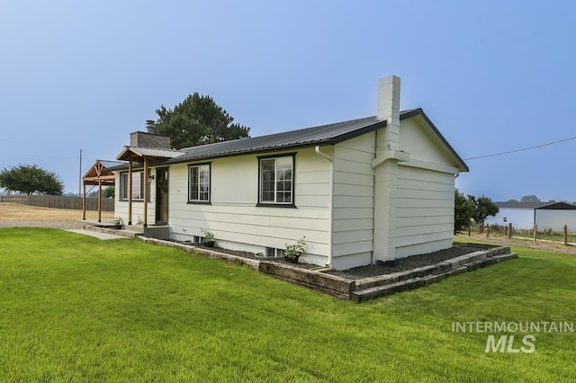 view of side of home with a lawn, a chimney, metal roof, and fence