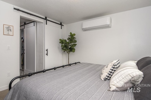 bedroom with a barn door, carpet, a wall unit AC, baseboards, and a textured ceiling