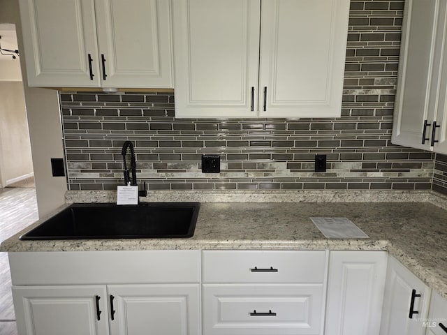 kitchen with light stone counters, a sink, white cabinetry, and decorative backsplash