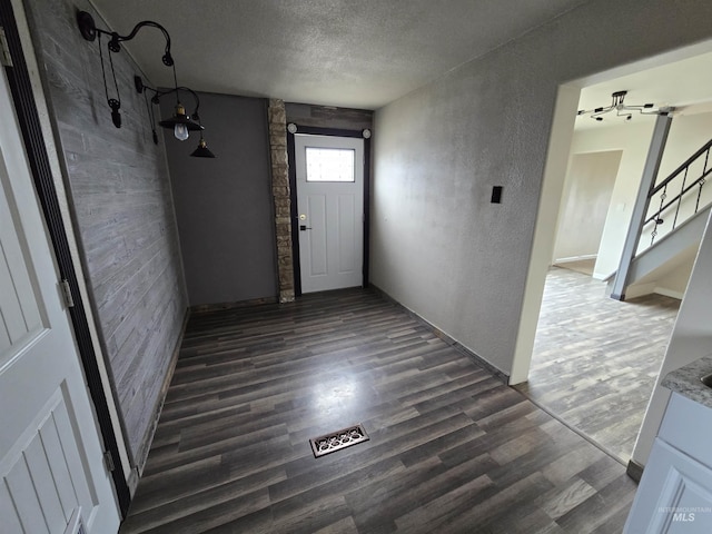 entryway with stairway, dark wood-style flooring, a textured ceiling, and a textured wall