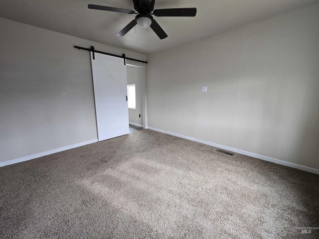 spare room with a barn door, visible vents, baseboards, ceiling fan, and dark colored carpet