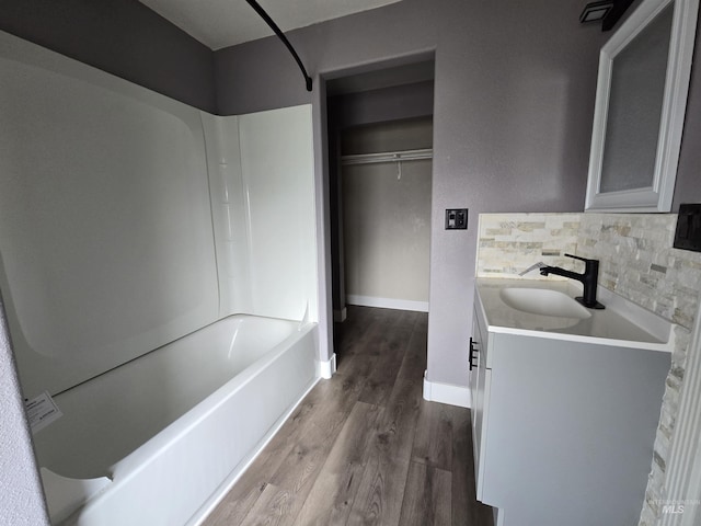 full bathroom featuring baseboards, wood finished floors, bathtub / shower combination, vanity, and backsplash