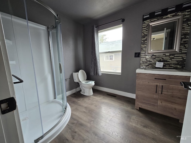 bathroom featuring tasteful backsplash, a shower stall, vanity, wood finished floors, and baseboards