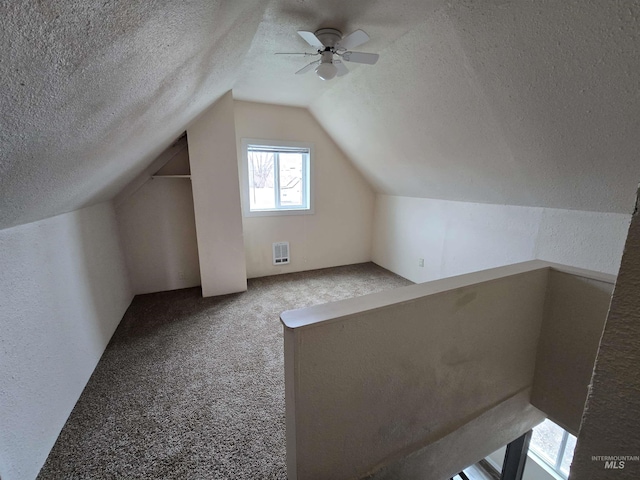 bonus room with a textured ceiling, a textured wall, carpet floors, visible vents, and vaulted ceiling