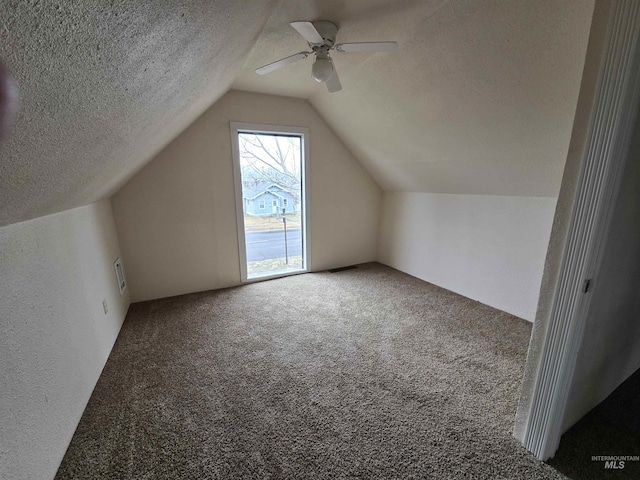 additional living space with a textured ceiling, vaulted ceiling, and carpet