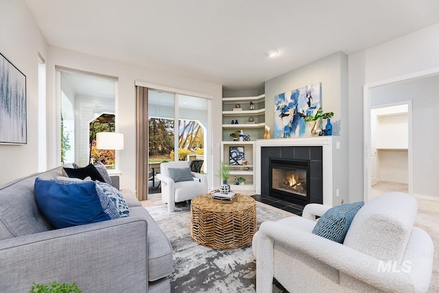 carpeted living room featuring built in shelves and a tiled fireplace