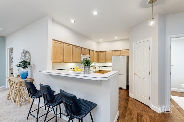 kitchen with light brown cabinets, hanging light fixtures, dark hardwood / wood-style flooring, white refrigerator, and kitchen peninsula