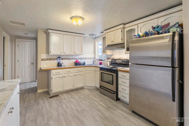 kitchen featuring light wood-type flooring, appliances with stainless steel finishes, a textured ceiling, and decorative backsplash