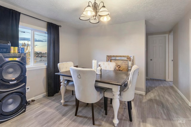 dining space with light hardwood / wood-style floors, a textured ceiling, and an inviting chandelier