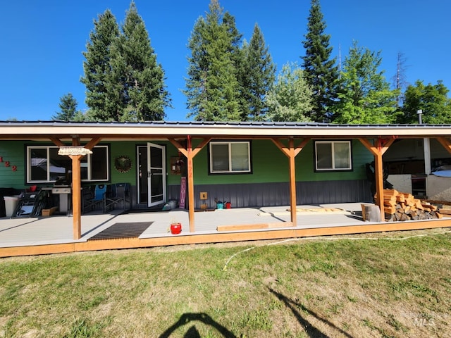 rear view of property featuring metal roof, a deck, and a yard